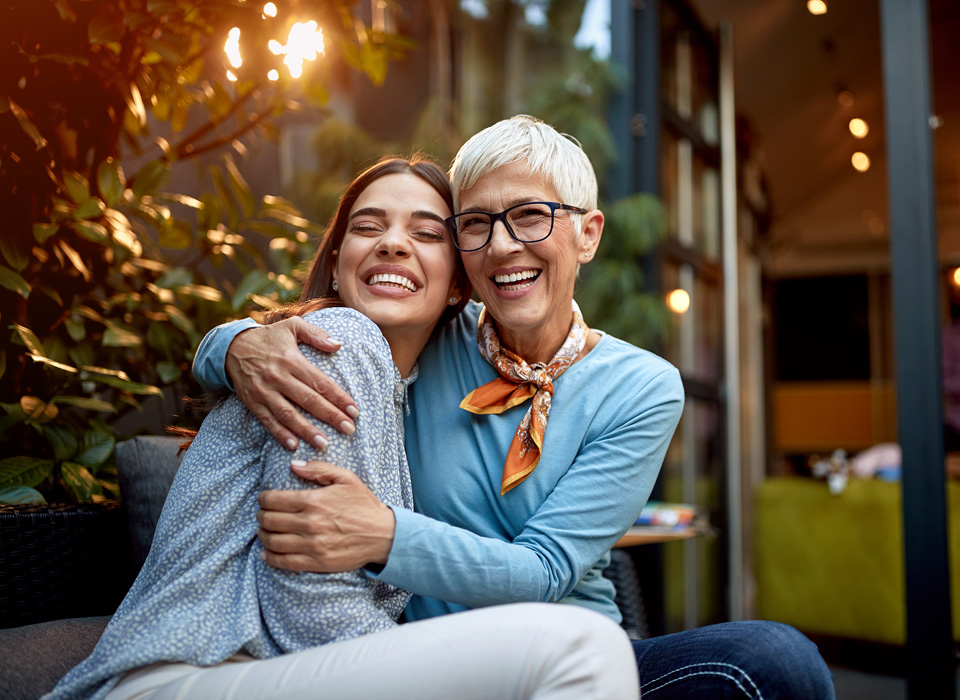 Portrait of a senior mother and adult daughter, hugging and smiling.